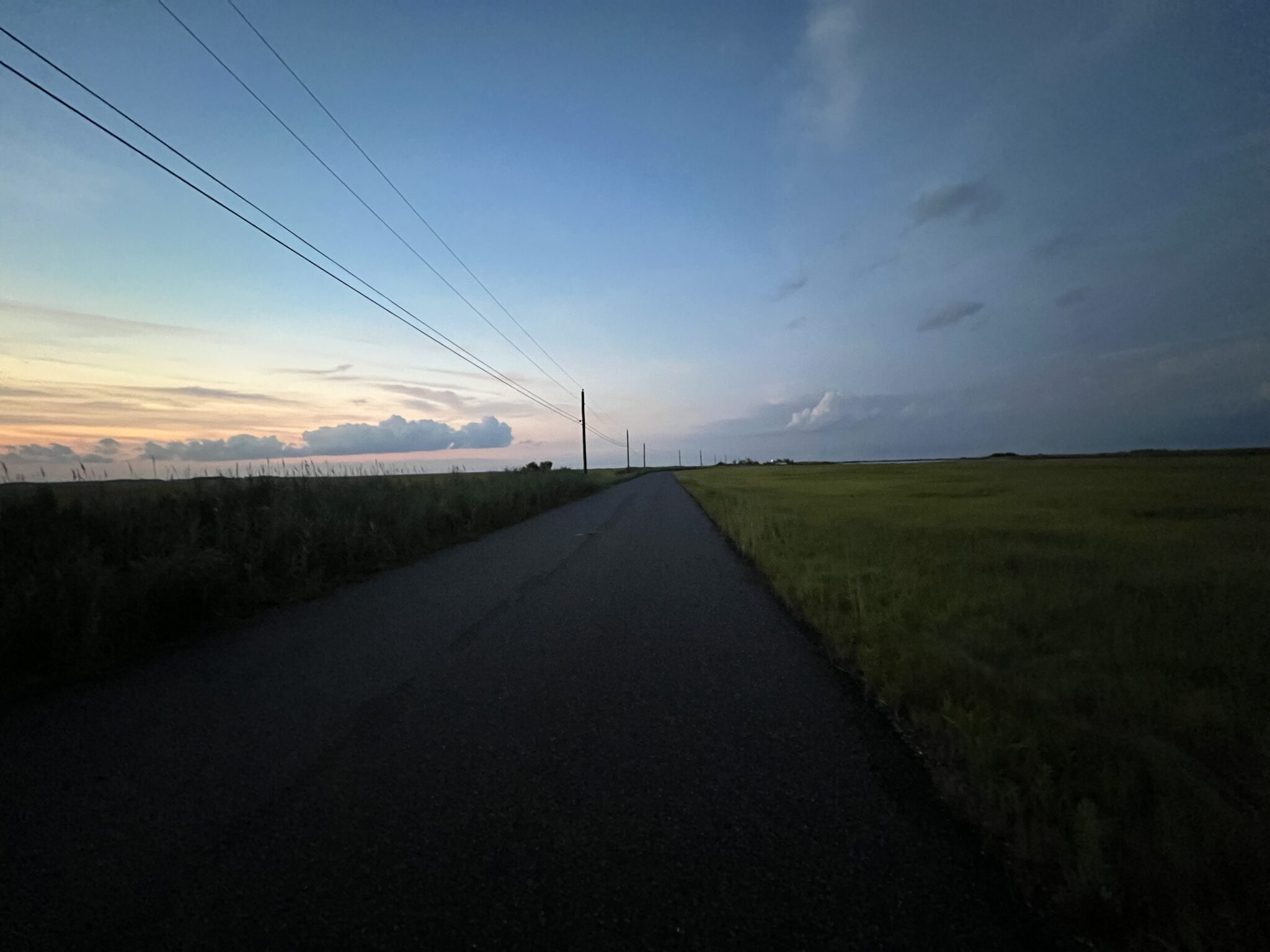 An empty stretch of road at sunset, bordered by open salt marsh.